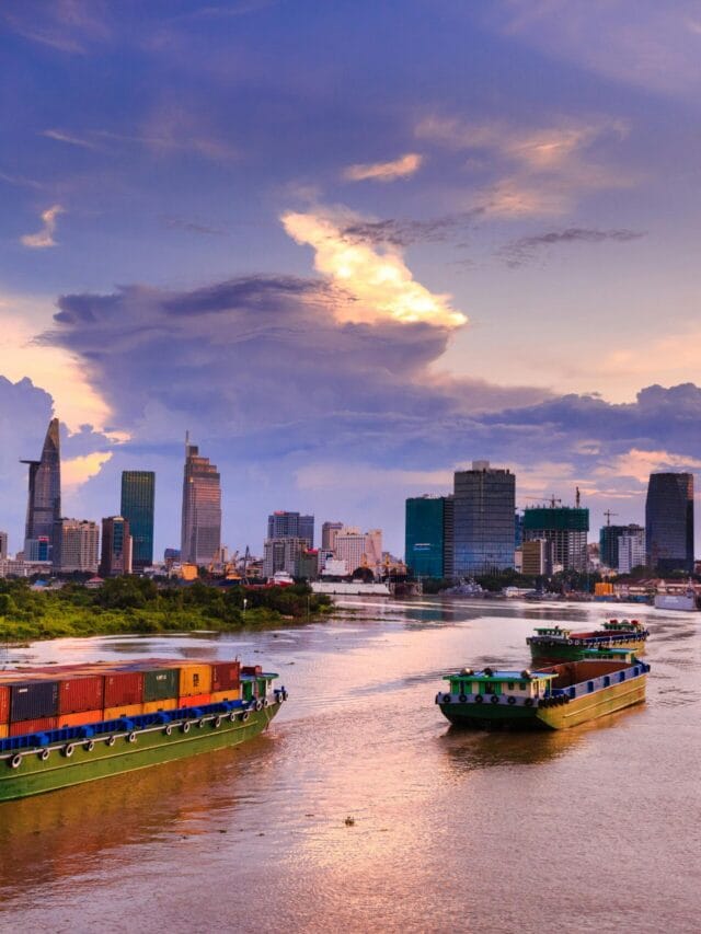 Container ships navigate the scenic Saigon River with Ho Chi Minh City skyline at dusk.